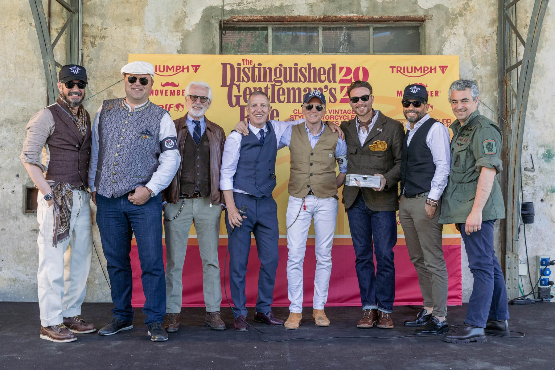 Il team dei Wheelers all'arrivo del DGR Milano 2025, in posa davanti al backdrop ufficiale dell'evento